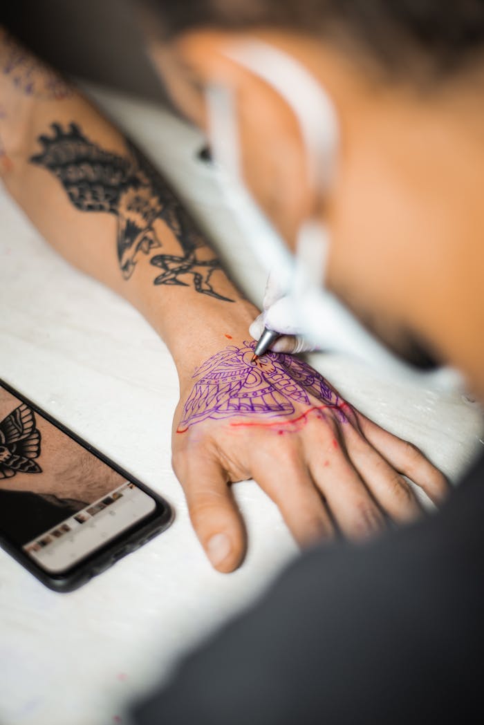 Detailed view of a tattoo artist working on a hand tattoo in a studio.