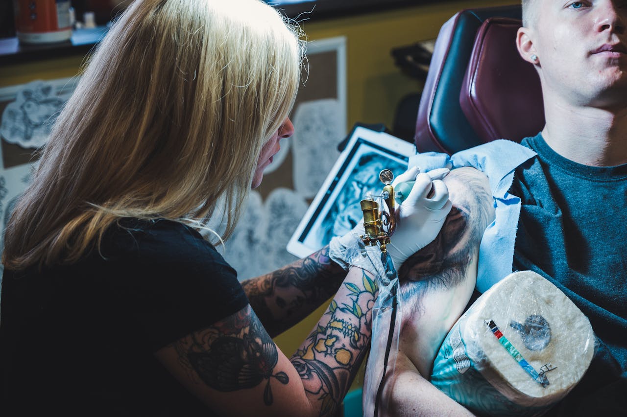A tattoo artist concentrates while creating a detailed tattoo design on a client's arm in a studio setting.