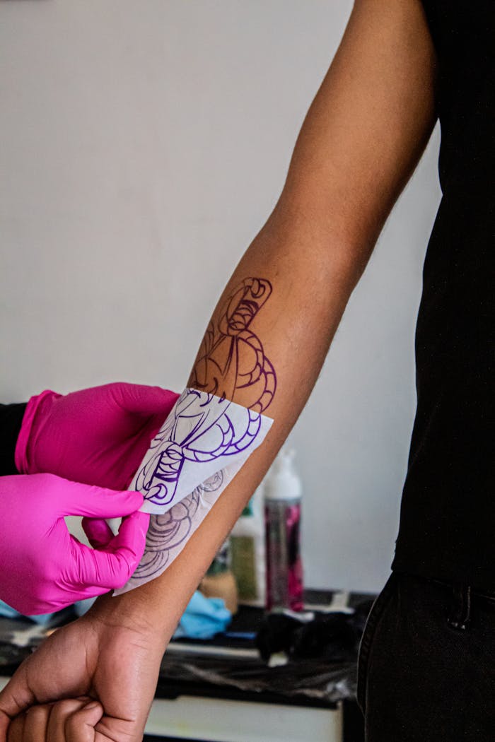 A tattoo artist places a stencil on a client's arm, preparing for tattooing in a studio setting.
